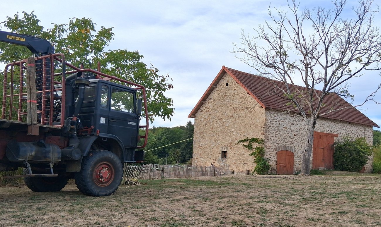 Camion forestier à grue devant une grange en pierre
